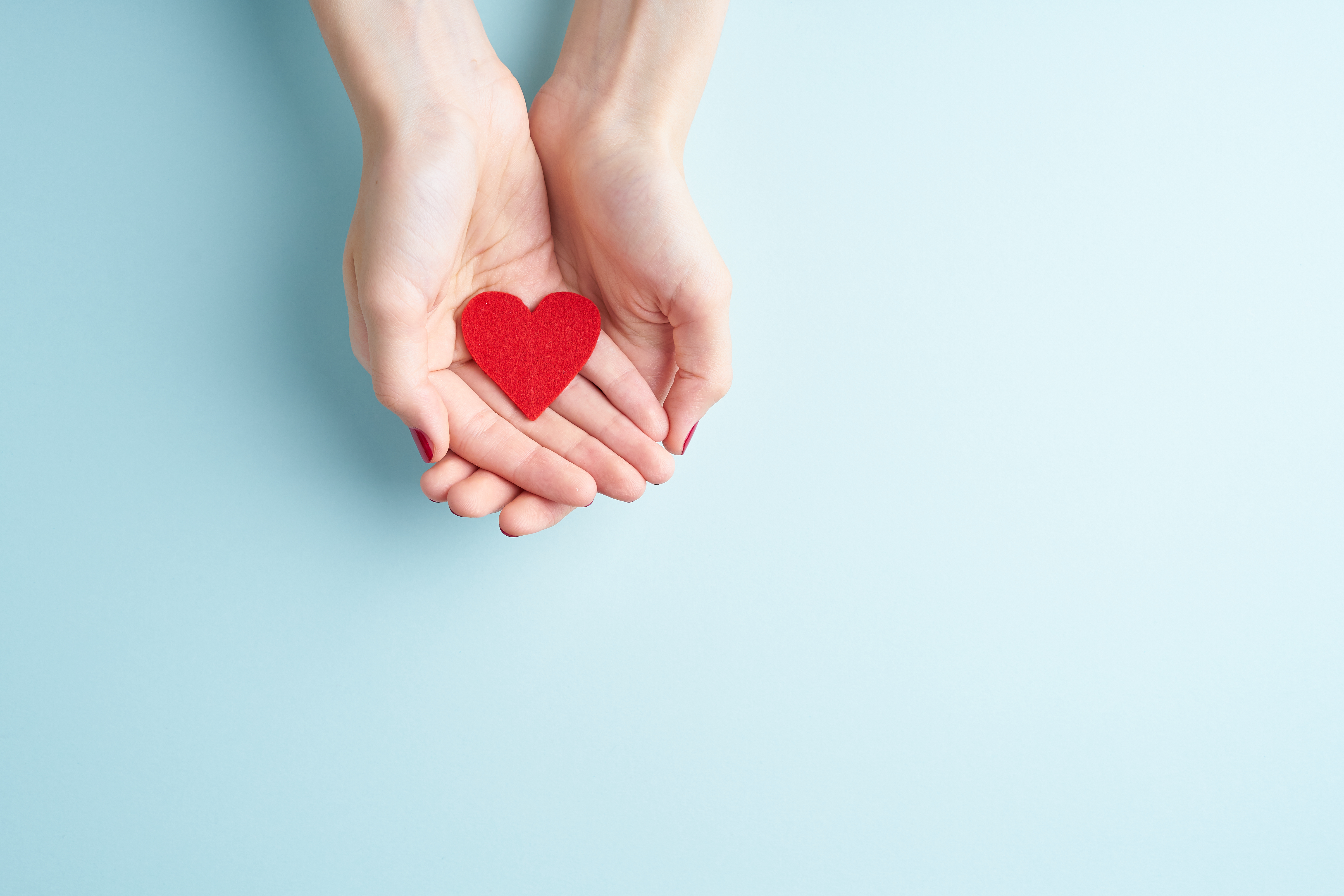 Cupped hands holding a paper heart.